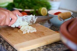 detailopname chef-kok handen hakken ui Aan houten snijdend bord, voorbereidingen treffen avondeten Bij huis foto