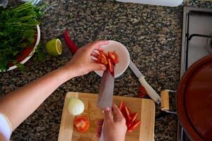 visie van bovenstaand van een chef snijden groenten, toevoegen gehakt tomaten in een wit salade kom foto