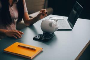 jong Aziatisch vrouw besparing voor pensioen besparing geld door een varkentje bank en nemen aantekeningen Aan notitieboekje, spaargeld concept. foto