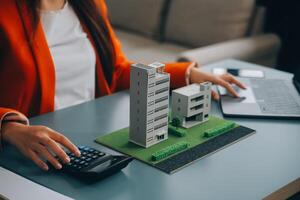 dichtbij omhoog makelaar zitten Bij tafel houdt klein huis model, lay-out van huisje. echt landgoed aankoop, nieuw eigendom, eigendom, bouw bedrijf maken speciaal aanbod naar cliënt, betaalbaar woning concept foto