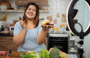 Aziatisch zwanger blogger op zoek Bij smartphone camera, ze is leven streaming Koken klasse voor zwanger. Aziatisch vrouw staand gelukkig glimlachen Bij de keuken teller voorbereidingen treffen vers biologisch salade. foto