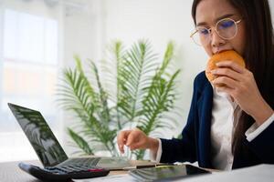 bezig en moe zakenvrouw aan het eten brood en melk voor lunch Bij de bureau kantoor en werken naar leveren financieel verklaringen naar een baas. overwerkt en ongezond voor klaar maaltijden, burn-out concept. foto