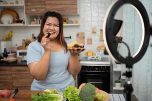 Aziatisch zwanger blogger op zoek Bij smartphone camera, ze is leven streaming Koken klasse voor zwanger. Aziatisch vrouw staand gelukkig glimlachen Bij de keuken teller voorbereidingen treffen vers biologisch salade. foto