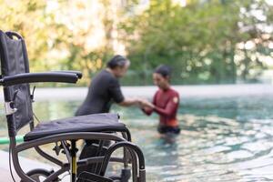 selectief focus uit rolstoel achtergrond van fysiek therapeut helpen senior vrouw in water, oud Dames en volwassen aan het doen aqua aerobics oefening in zwemmen zwembad, ouderen sport, en actief levensstijl. foto