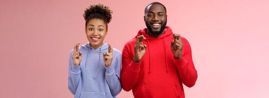 Lucky charmant aantrekkelijk positief Afro-Amerikaans vrienden vent meisje kruis vingers maken wens glimlachen breed opgewonden van mening zijn trouw droom komen waar Hopelijk kijken camera, anticiperen wonder foto