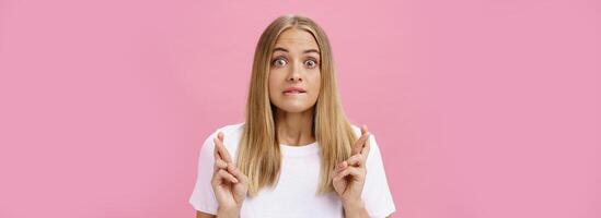 opgewonden en opgewonden aantrekkelijk emotioneel blond haar vrouw met puistjes Aan voorhoofd bijten lager lippen kruispunt vingers voor mooi zo geluk maken wens bidden verlangen worden realiteit over- roze muur foto