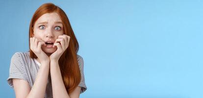 bang sprakeloos verbijsterd bang roodharige meisje beven angst breed ogen doodsbang bijten vingernagels fronsen beven angstig staand blauw achtergrond hijgen geschokt foto