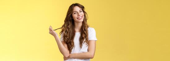 dwaas schattig vrouwelijk sensueel krullend haar vrouw kantelen hoofd spelen haar- strand rollend krullen glimlachen verheugd geïnteresseerd luisteren flirterig gesprek koket staren camera staan geel achtergrond foto