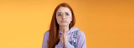 alstublieft smeken jij. windend van streek verdrietig Kaukasisch roodharige vriendin vervelend bril fronsen grimassen pruilen pleiten helpen vragen gunst nodig hebben dringend lenen iets, oranje achtergrond foto