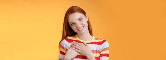 verheugd inschrijving vrouwelijk mooi roodharige vrouw te ontvangen compliment bekentenis tintje hart voelen warmte liefste moment glimlachen verheugd lief houden liefde binnen ziel, staand oranje achtergrond foto