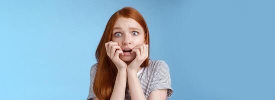 bang sprakeloos verbijsterd bang roodharige meisje beven angst breed ogen doodsbang bijten vingernagels fronsen beven angstig staand blauw achtergrond hijgen geschokt foto