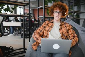 Kaukasisch hipster vent genieten van afstand baan in koffie winkel, mannetje freelancer in modieus bril zittend in cafetaria met modern laptop apparaat foto