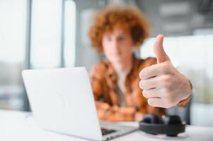 jong gelukkig mannetje freelancer in gewoontjes kleren zittend in cafe met laptop en gebruik makend van mobiel telefoon. foto