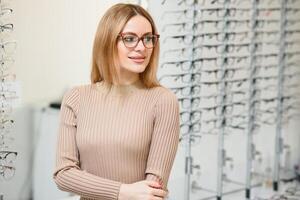 Gezondheid zorg, gezichtsvermogen en visie concept - gelukkig vrouw kiezen bril Bij optiek op te slaan. portret van mooi jong vrouw proberen nieuw bril in opticien op te slaan. foto