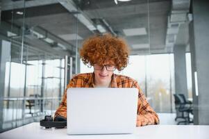 Kaukasisch hipster vent genieten van afstand baan in koffie winkel, mannetje freelancer in modieus bril zittend in cafetaria met modern laptop apparaat foto