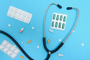 verspreide wit pillen Aan blauw tafel.medisch, apotheek en gezondheidszorg concept. blauw achtergrond wit pillen met een medisch statoscoop, top visie foto
