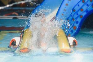 de jongen is rollend met een water glijbaan Bij een water park in weinig rots foto