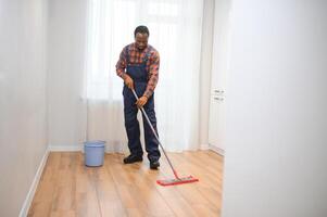 jong Afrikaanse Mens wast de verdieping met een dweilen in de kamer foto