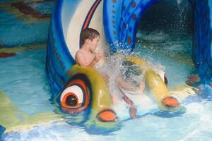 de jongen is rollend met een water glijbaan Bij een water park in weinig rots foto