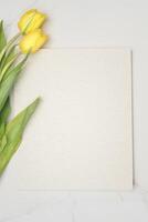 blanco perkament papier Aan wit marmeren met geel tulpen foto