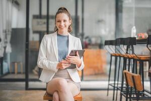 bedrijf vrouw concept, gezeten comfortabel in een kantoor omgeving, een zakenvrouw met een aangenaam glimlach toepassingen een digitaal tablet voor haar werk. foto