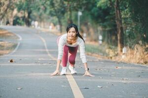 sport geschiktheid concept, een gefocust jong vrouw in sportkleding krijgt klaar naar begin haar rennen Aan een vredig met bomen omzoomd weg. foto