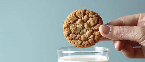 ai gegenereerd detailopname van een hand- Holding een koekje, glas van melk. reeks tegen een levendig blauw achtergrond, helder verlichting verbetert de verwachting van de dompelen moment. foto