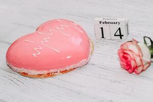 roze thee roos met hart vormig roze mousse taart en februari 14 kalender. foto