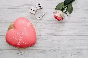 roze thee roos met hart vormig roze mousse taart en februari 14 kalender. foto