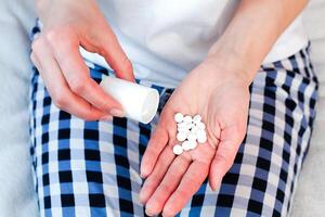 vrouw gieten pillen van een fles in haar hand. nemen vitamines, supplementen, antibiotica, antidepressiva, pijnstiller medicatie. detailopname. foto