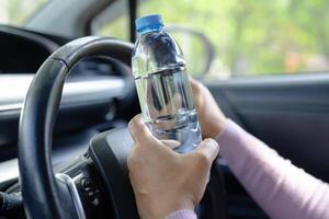 Aziatische vrouw die een fles vasthoudt om water te drinken tijdens het autorijden. plastic warmwaterkruik brand veroorzaken. foto