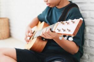 Aziatisch jongen spelen gitaar in de huis. muziek- aan het leren concept, muziek- vaardigheid opleiding foto