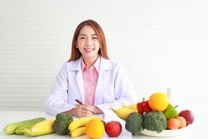 mooi Aziatisch voedingsdeskundige zittend Bij haar bureau met fruit en groenten ze gaf advies en bereiden voedzaam voedsel eten schoon, gezond voedsel. Gezondheid zorg concept foto