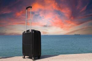 een koffer is staand Aan een strand met een zonsondergang in de achtergrond. reis, vakantie en vakantie begrip. zomer tijd. foto