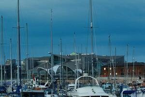 jachthaven met zeilboten aangemeerd Bij schemering, modern gebouwen in de achtergrond onder een bewolkt lucht. foto