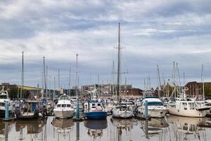 rustig jachthaven met afgemeerd zeilboten reflecterend Aan kalmte water, bewolkt lucht achtergrond. foto