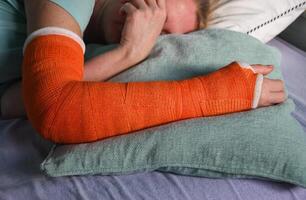 vrouw met een gebroken Rechtsaf arm met een oranje glasvezel gips gips slaapt in bed met een hoofdkussen onder de gips foto