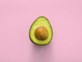 voor de helft van avocado Aan roze achtergrond, top visie. minimaal voedsel concept foto