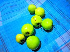 een groep van groen appels zittend Aan een blauw en wit geruit tafel kleding foto