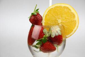 een glas van water met aardbeien en een oranje plak foto
