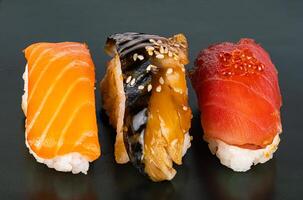 detailopname visie van drie soorten van vis sashimi sushi Aan donker achtergrond. hoog hoek visie van Japans zeevruchten sushi Aan zwart. foto