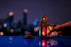 lantaarn Holding door hand- en klein bord van datums fruit Aan tafel met nacht lucht en stad bokeh licht achtergrond voor de moslim feest van de heilig maand van Ramadan kareem. foto