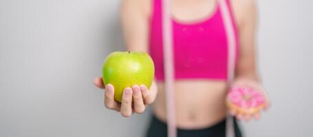 vrouw hand- houden groen appel en donut, vrouw geschiktheid Kiezen tussen fruit is gezond en zoet is ongezond rommel voedsel. dieet controle, gewicht verlies, zwaarlijvigheid, aan het eten levensstijl en voeding concept foto