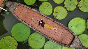 Aziatisch vrouw ontspannende Aan een lang staart boot omringd door reusachtig Victoria waterlelies in tropisch regenwoud Bij phuket Thailand foto