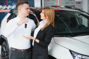 bezoekende auto dealerschap. mooi paar is Holding een sleutel van hun nieuw auto en lachend, meisje is zoenen haar man in wang. foto