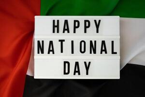 tekst gelukkig nationaal dag Aan achtergrond golvend vlag van vae. nationaal vakantie van Verenigde Arabisch emiraten. herdenking dag moslim Arabisch vakantie. Dubai viering foto