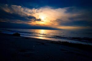 zonsondergang, verlichte zee. zanderig strand in de voorgrond. licht golven. Baltisch zee foto