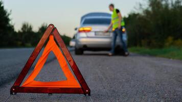 gebroken zilver luxe auto noodgeval ongeluk. Mens bestuurder installeren rood driehoek hou op teken Aan weg. sport auto- draaide zich om Aan oogkleppen technisch problemen Aan de weg. veiligheid procedure wanneer hebben voertuig gebroken naar beneden foto