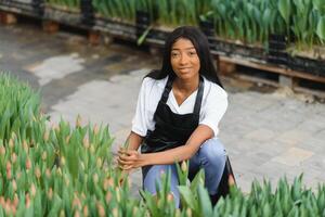 schattig Afrikaanse vrouw bloemist controle bloemen staat in kas foto