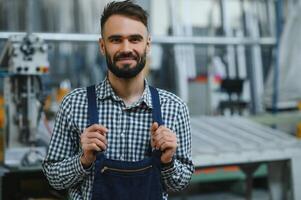 gelukkig professioneel zwaar industrie ingenieur arbeider vervelend uniform, en moeilijk hoed in een staal fabriek. glimlachen industrieel specialist staand in een metaal bouw vervaardiging foto